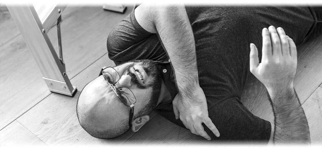 Black and white photo of a man lying on the floor clutching his shoulder in pain.