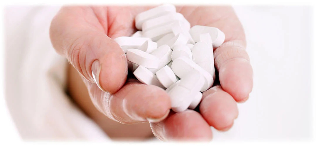 A close-up image of supplements in a cupped hand, suggesting the concept of taking too many vitamins or supplements.