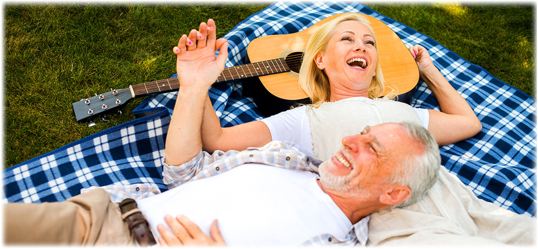 Joyful senior couple relaxing on picnic blanket with guitar, embodying Lily & Loaf's commitment to blissful wellness.