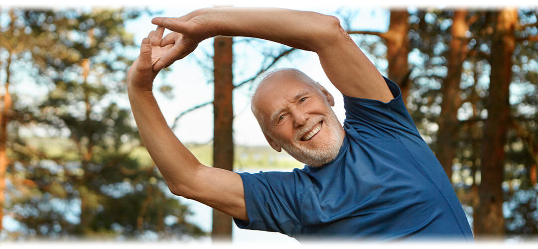 A person stretching their arms outwards while standing outdoors, with a bright sun shining in the background. The image conveys a sense of vitality and high energy levels