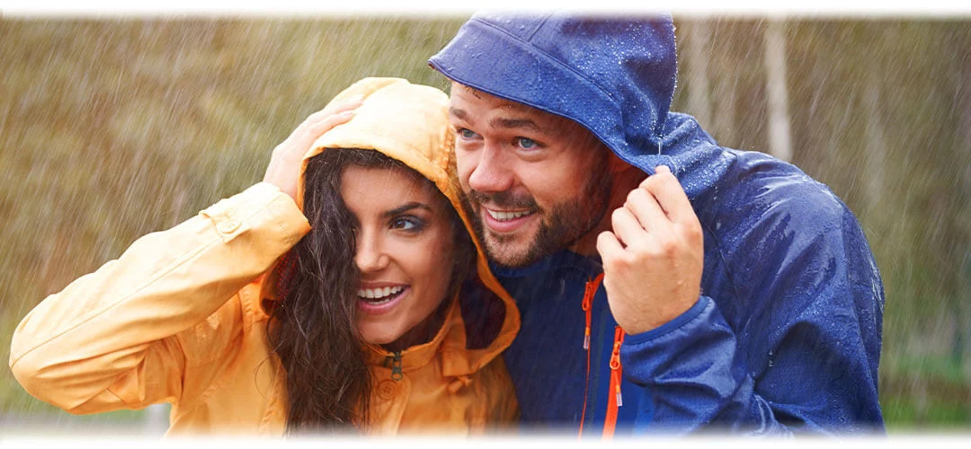 Man and woman sheltering under the hoods of their raincoats during a winter storm