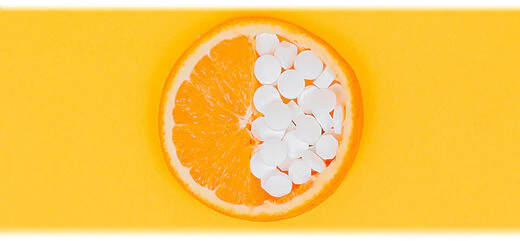 A colourful image of an orange slice where half is covered with supplements, representing vitamins and minerals for a healthy diet.