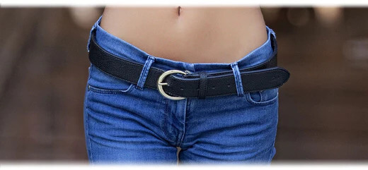 A person standing wearing loose jeans with a belt, representing successful weight loss.