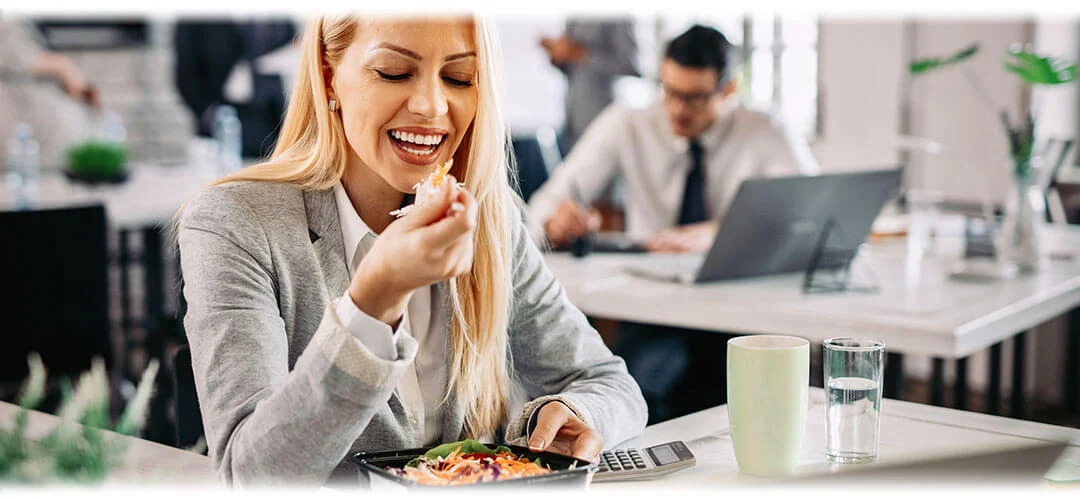A scene of a working lunch, with a person typing on a laptop while eating a salad and drinking water. The image represents the concept of a productive yet healthy meal during work hours.