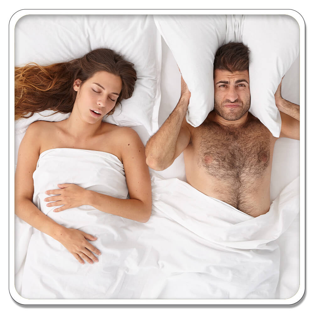 Man and woman sleeping in a bed. Man holding pillow over ears because woman snoring.