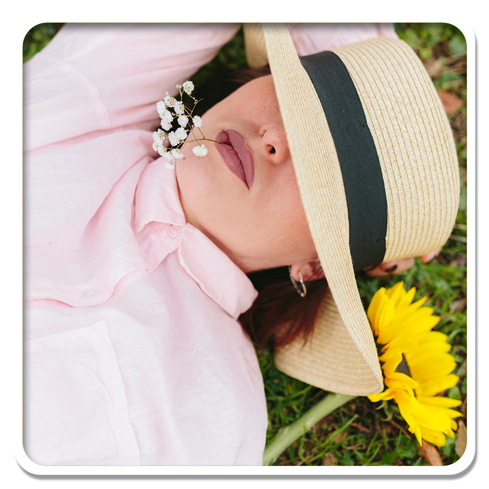 Relaxed woman lying in grass with a hat, enjoying nature's tranquility, inspired by Lily & Loaf.