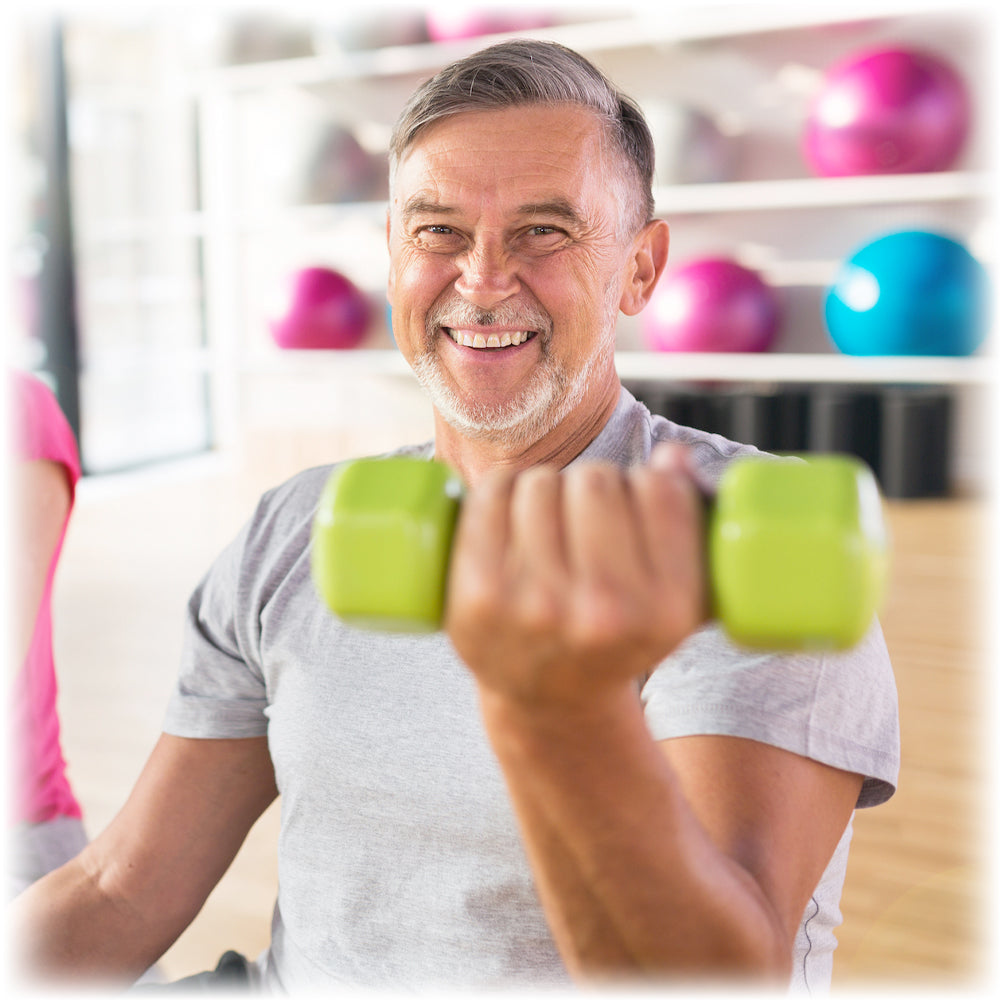 Smiling senior man lifting green dumbbells at gym, embodying Lily & Loaf's commitment to healthy aging and vitality
